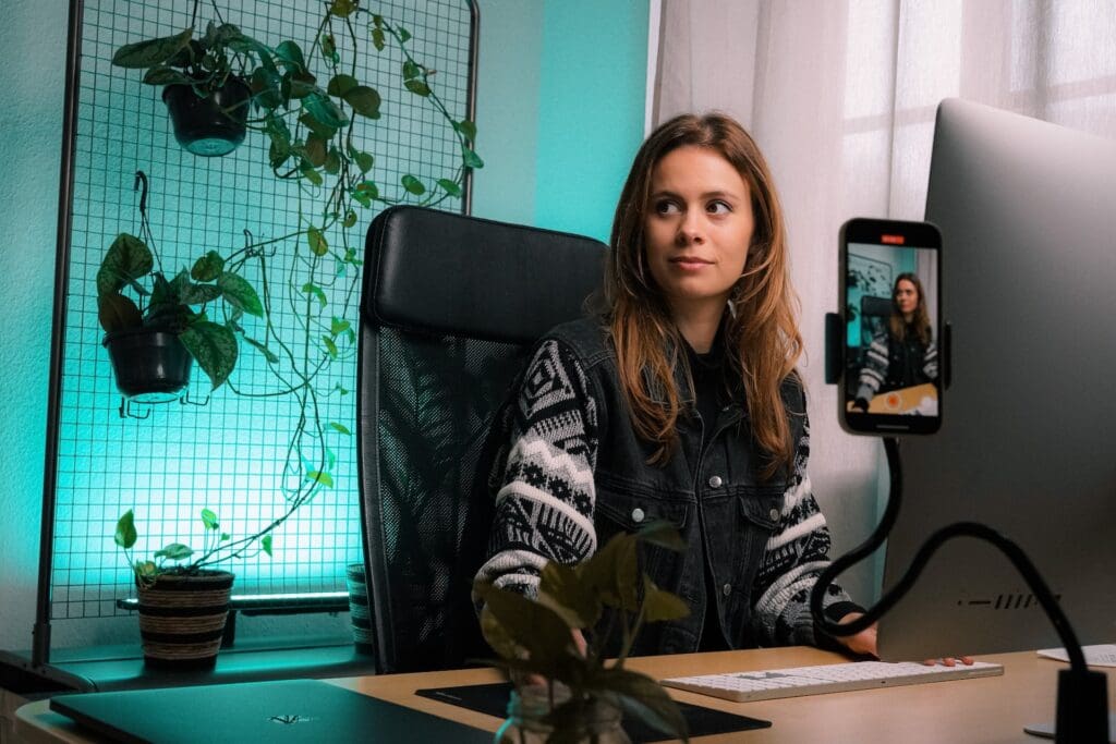 How to join the YouTube Partner Program: A YouTube content creator sits in front of her computer with a smartphone recording a video